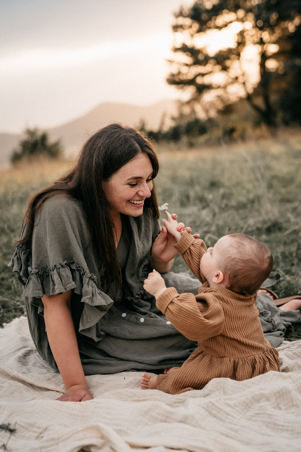 A one year old girl is giving a flower to her mother. Mother is smelling the flower and smiling.