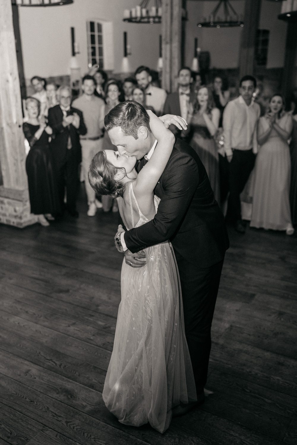 Brautpaar während ihres Hochzeitstanzes. Küssen sich und die Gäste jubeln im Hintergrund. 