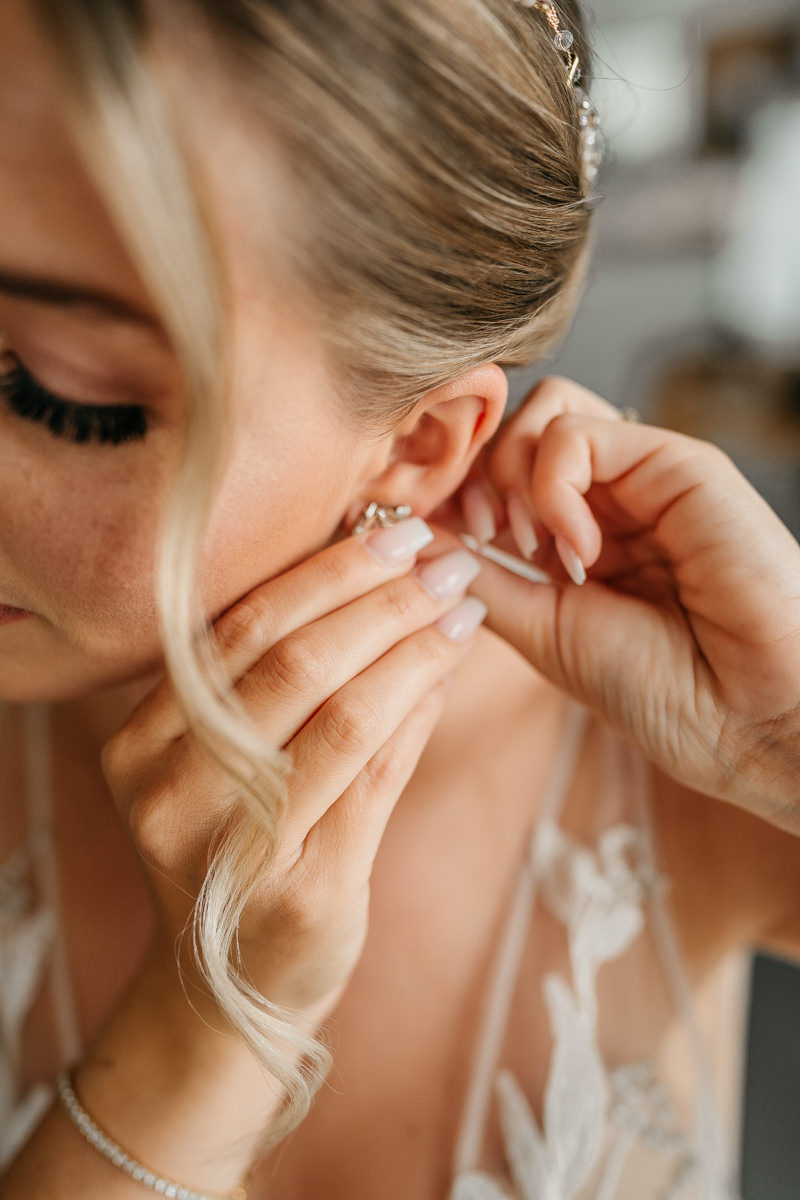 Braut zieht während ihres Getting Ready einen Ohring an. Das Foto zeigt ein Close up davon.