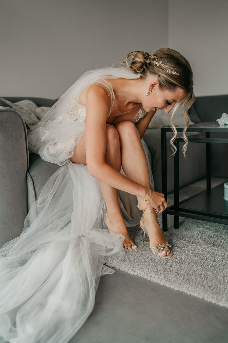 Braut während ihres Getting Ready. Sie zieht sich gerade die Schuhe an. 