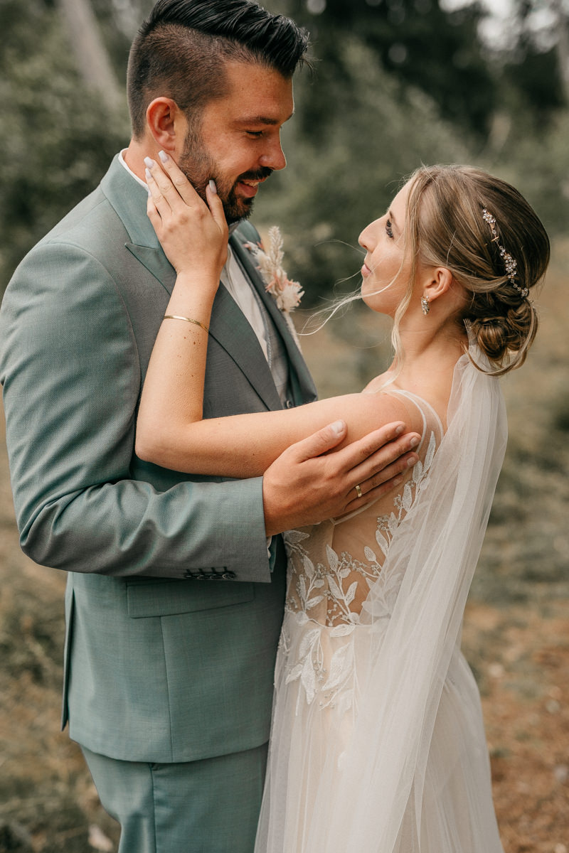 Brautpaar an ihrem Hochzeitstag. Braut streichelt das Gesicht des Bräutigam und schaut ihm tief in die Augen.