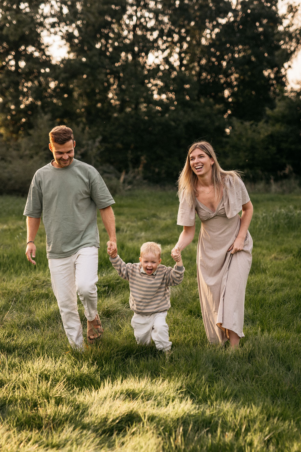 a man and woman holding hands and a baby walking in a grassy field