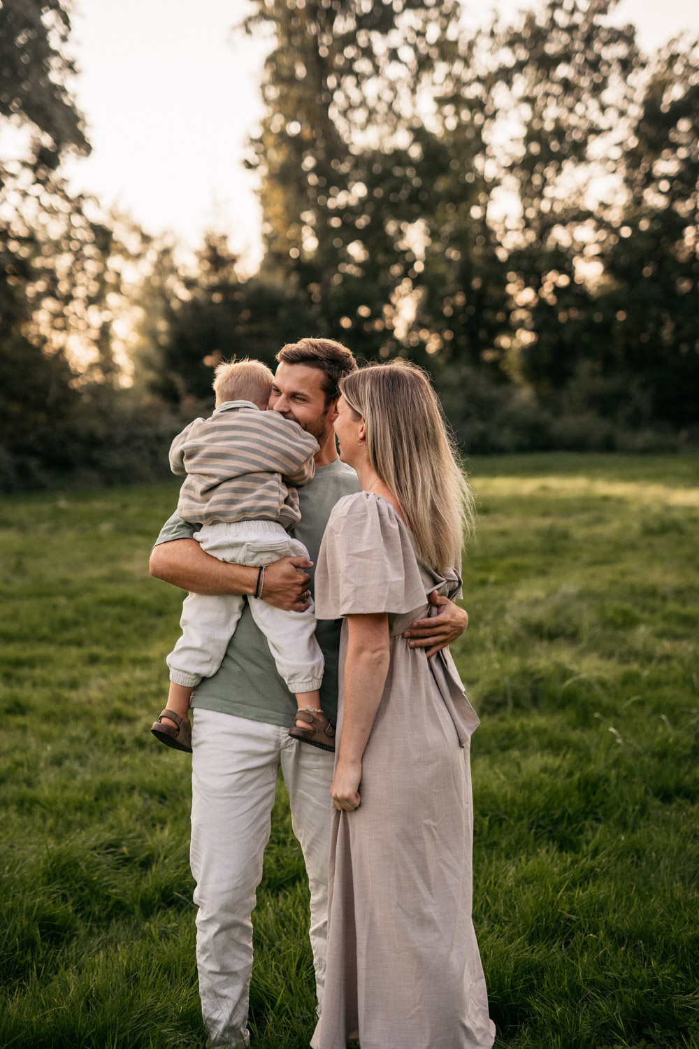 a man and woman holding a baby in a grassy field