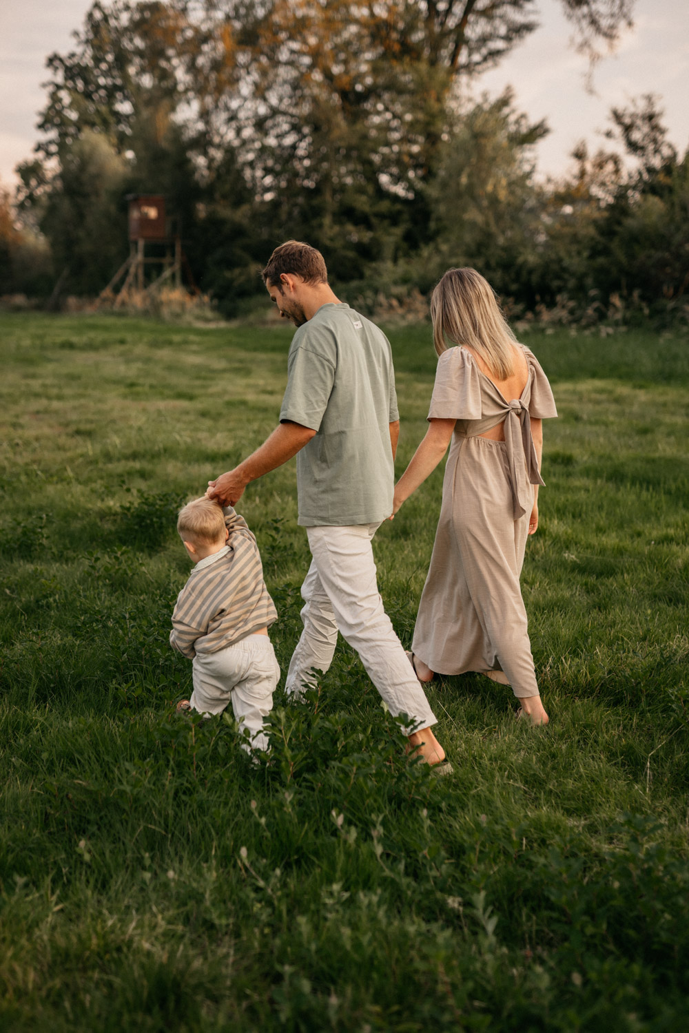 a man and woman holding hands and walking with a child in a grass field