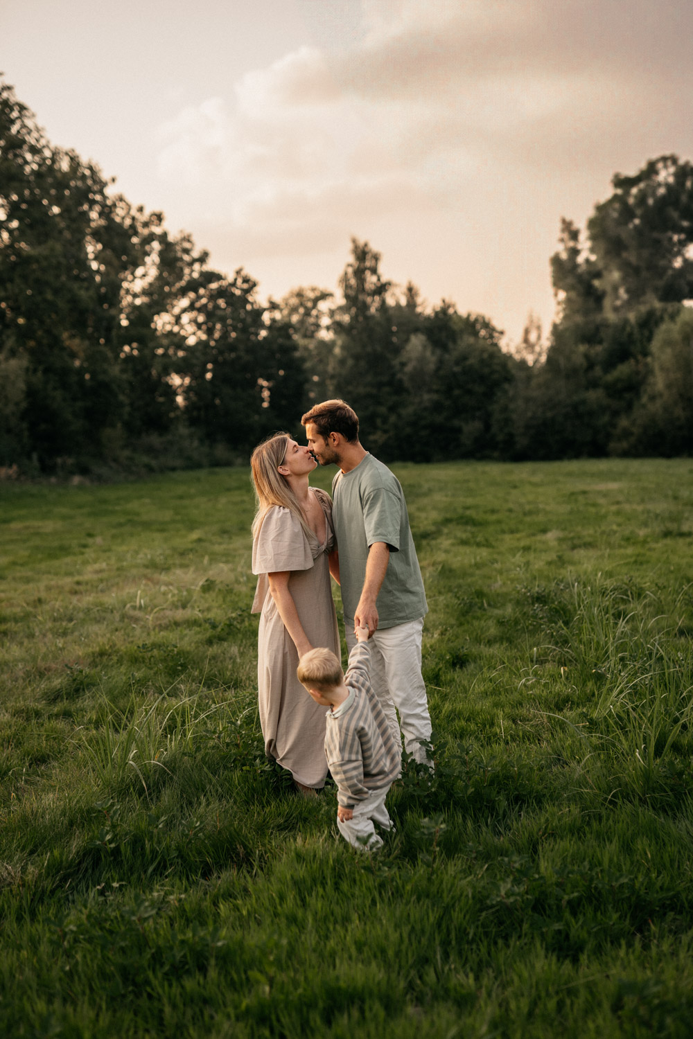 a man and woman kissing a child in a field