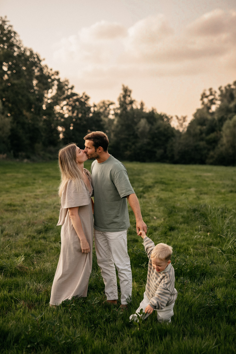 a man and woman kissing a child in a field