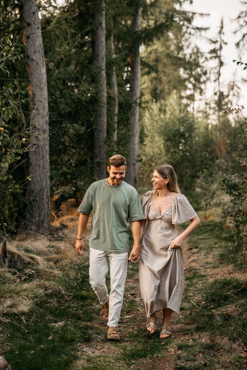 a man and woman holding hands and walking in the woods