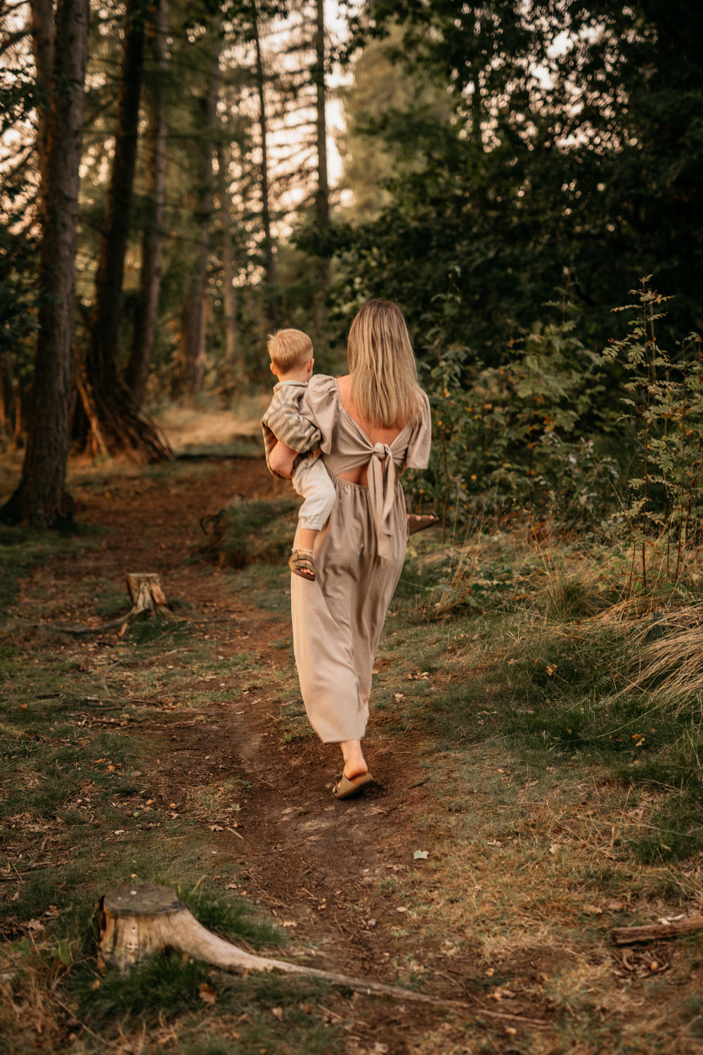 a woman carrying a baby walking on a path in the woods