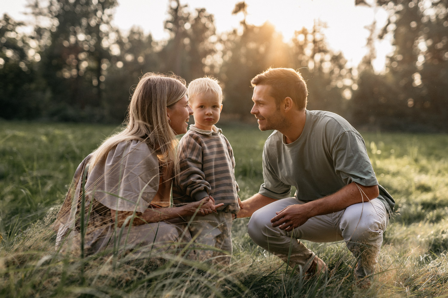 Eltern mit ihrem Kind beim Familienshooting auf einer Wiese. Im Hintergrund geht die Sonne unter.