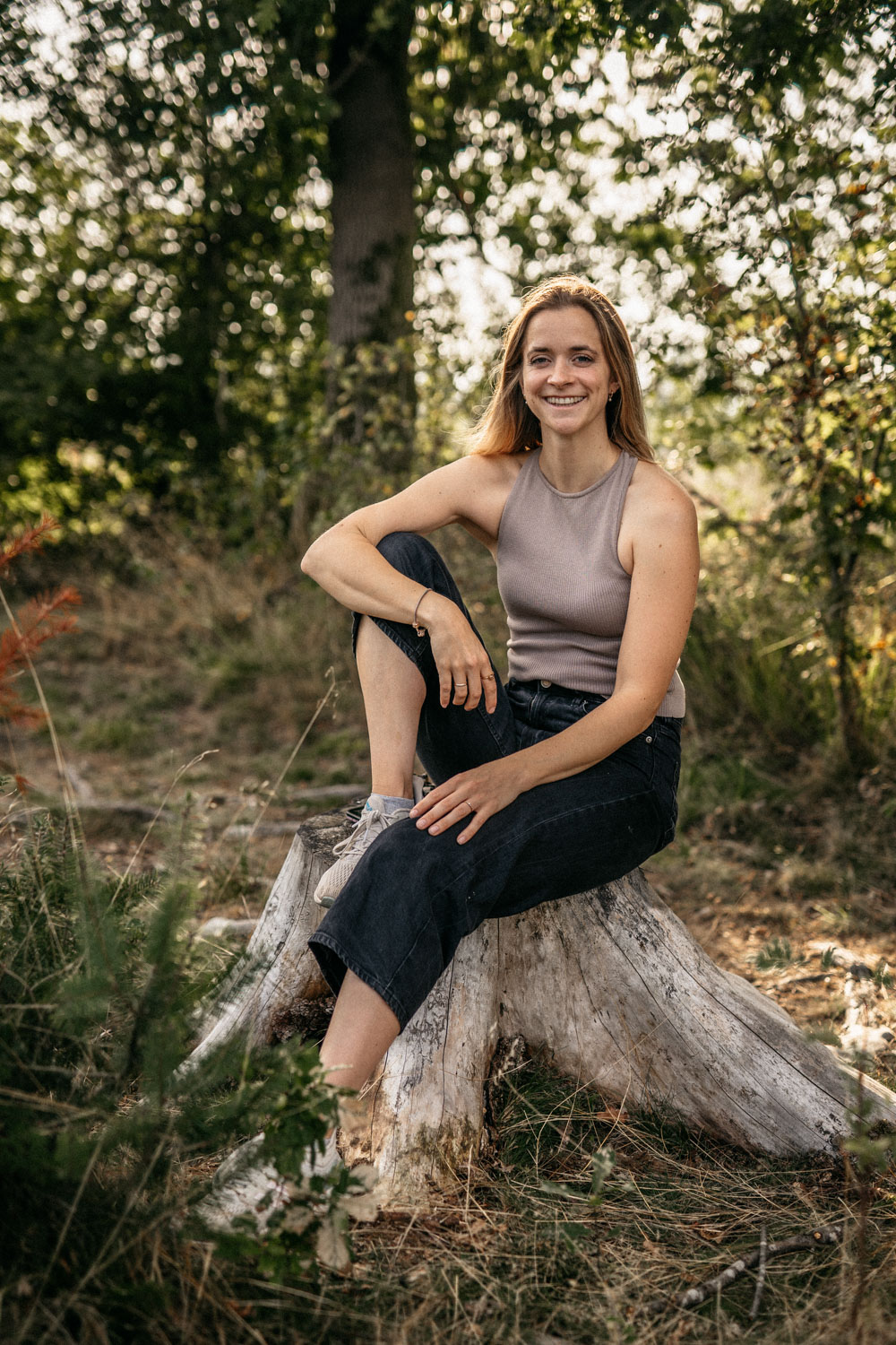 Selbstportrait. Theresa Moldenhauer, Hochzeitsfotografin aus Kassel, sitzt lässig auf einem Baumstumpf in der Natur. 